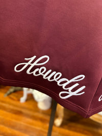 Maroon fabric with 'Howdy' embroidery on a wooden surface