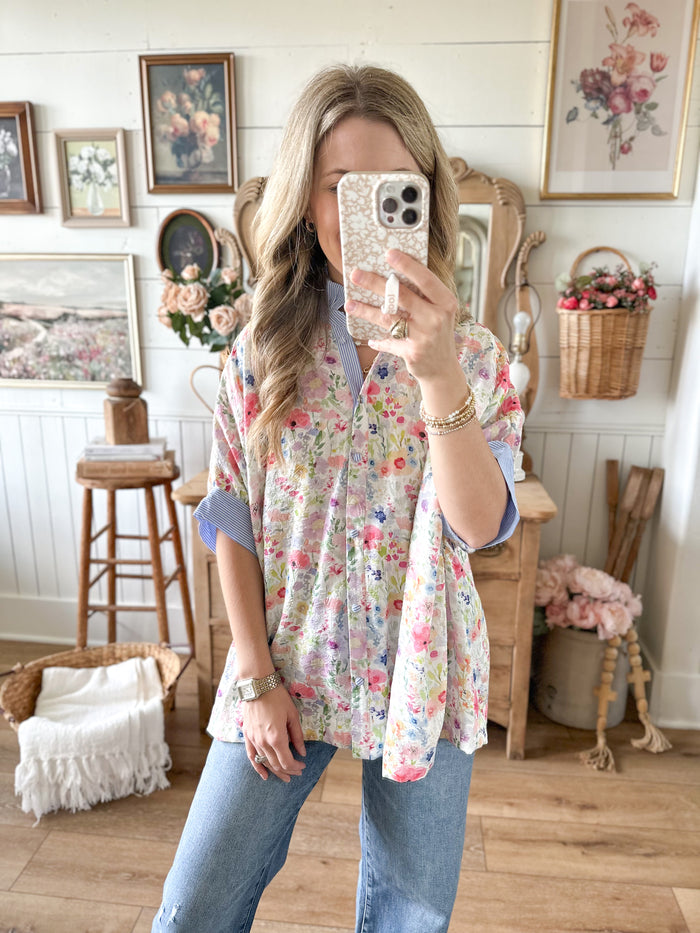 Woman taking a mirror selfie in a floral blouse and jeans in a home setting.