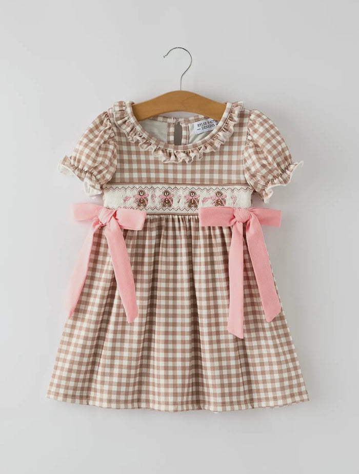 Checkered dress with pink ribbons on a hanger against a light gray background