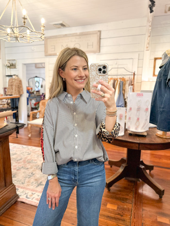 Woman taking a mirror selfie in a clothing store wearing a striped shirt and jeans.