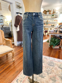 Blue jeans on a mannequin in a store setting with wooden floors and furniture.