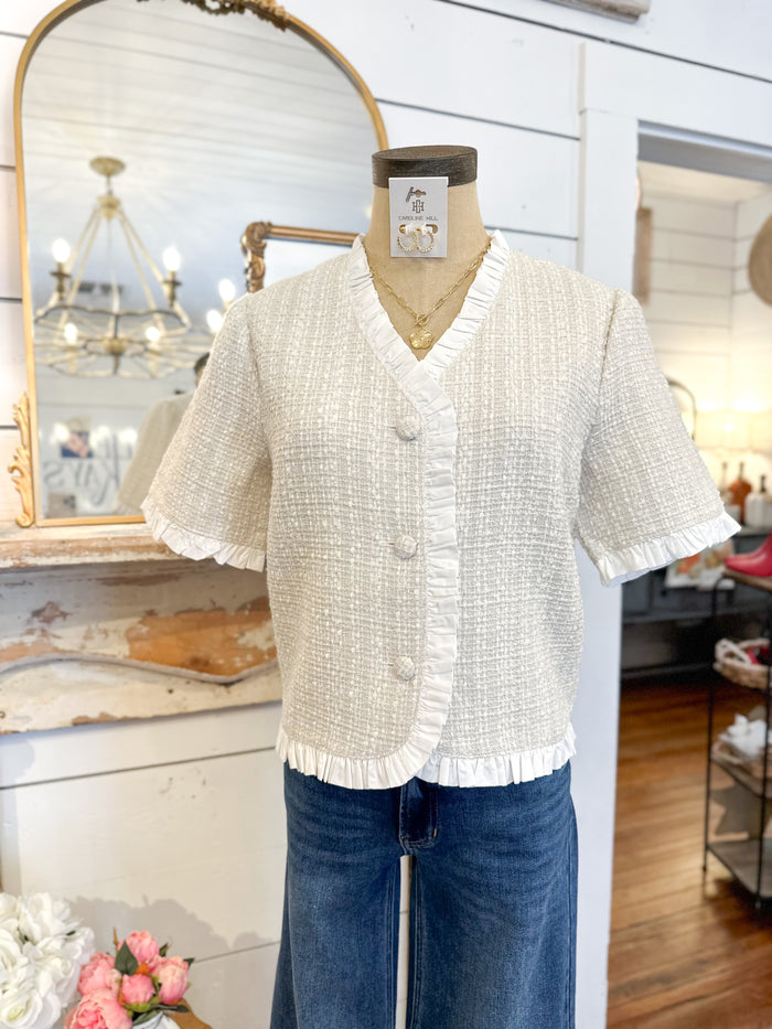White textured short-sleeve blouse on a mannequin with blue jeans in a store setting.
