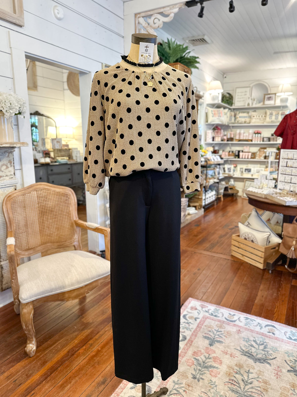 Mannequin wearing a polka dot blouse and black pants in a store setting