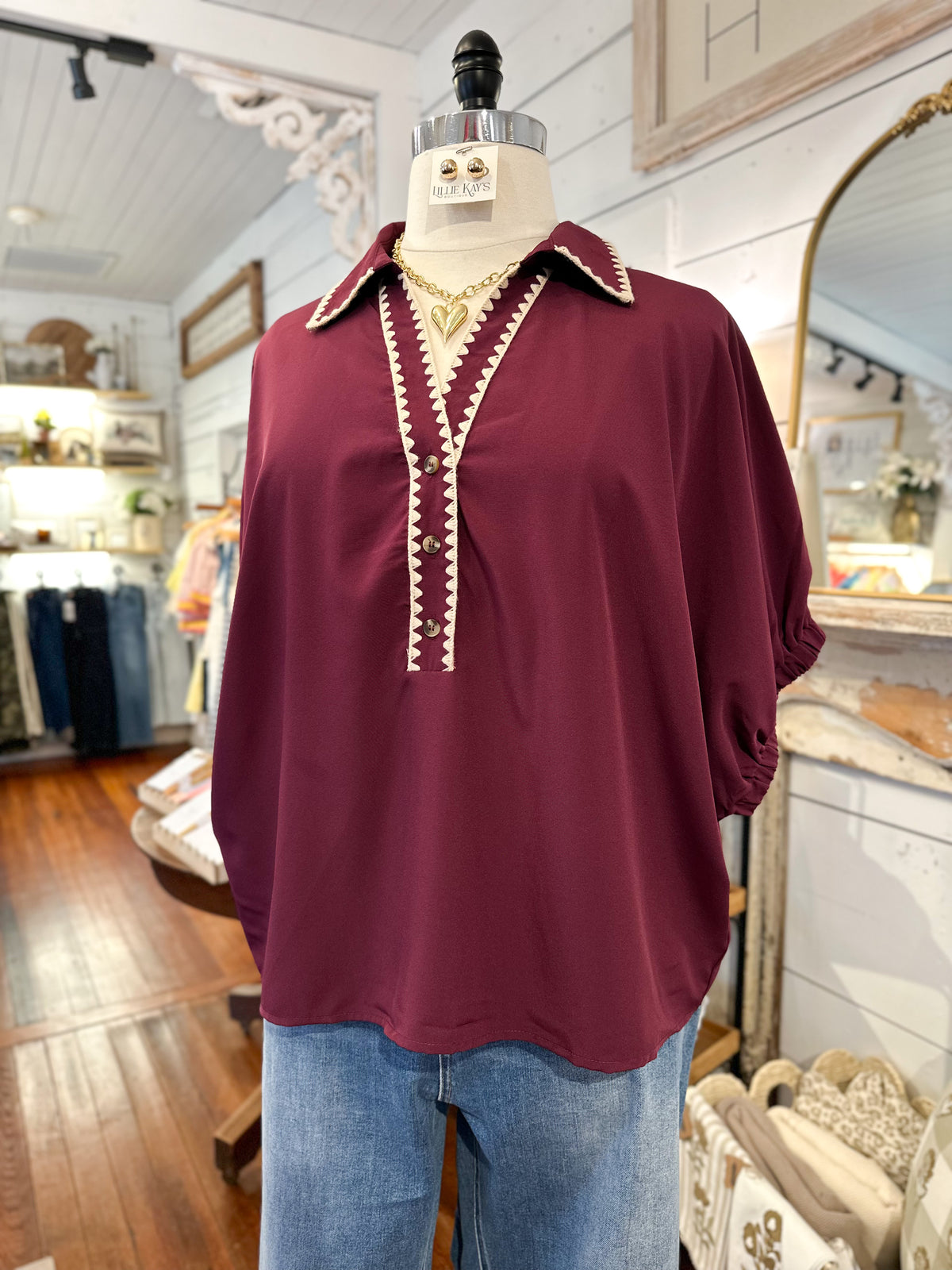 Maroon blouse with white trim on a mannequin in a store setting