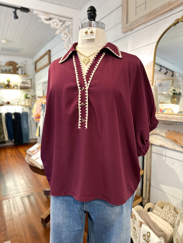 Maroon blouse with white trim on a mannequin in a store setting
