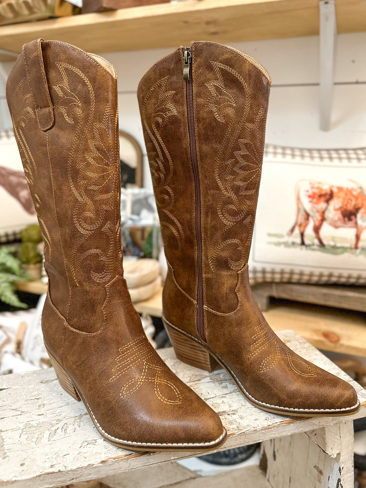 Pair of brown cowboy boots with intricate designs on a wooden surface.