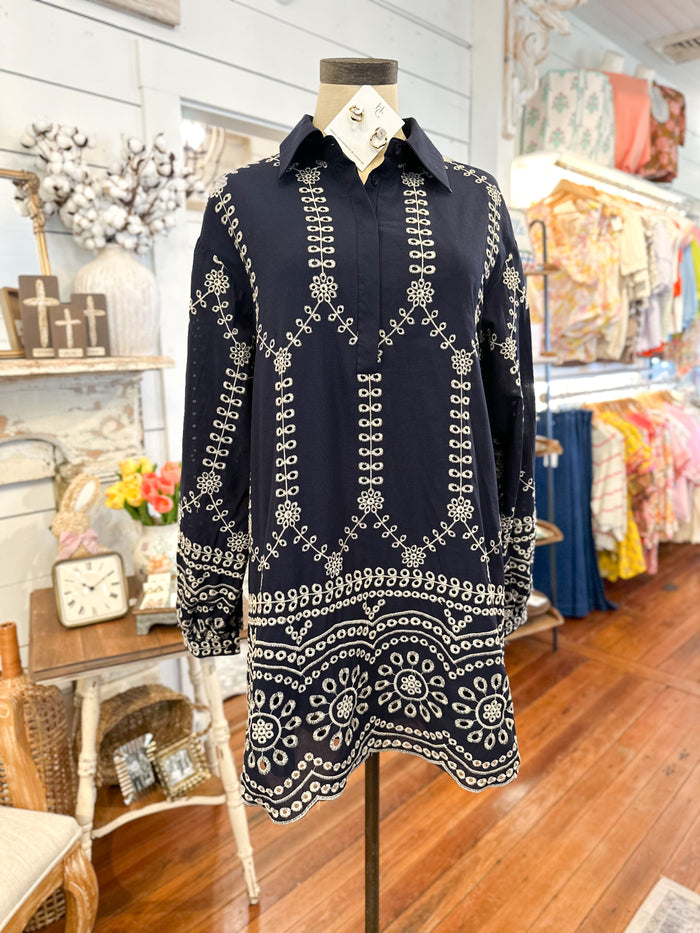Navy blue dress with intricate white patterns on a mannequin in a store setting.