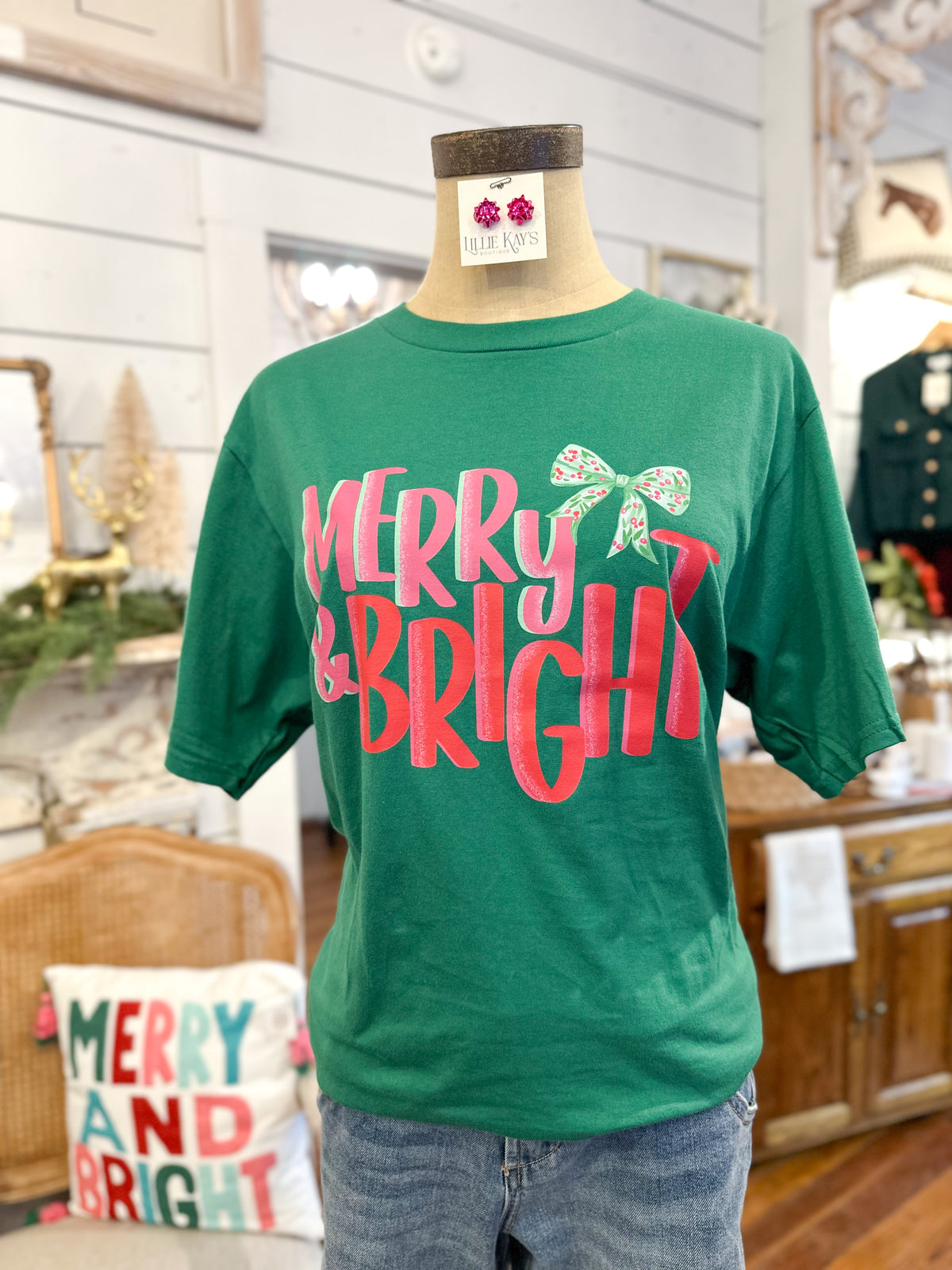 Green t-shirt with 'Merry & Bright' text on a mannequin in a festive indoor setting.