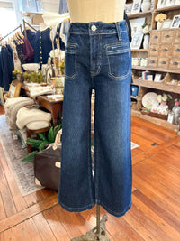 A pair of dark blue wide-leg denim jeans displayed on a mannequin torso inside a boutique shop with wooden floors and shelves in the background.