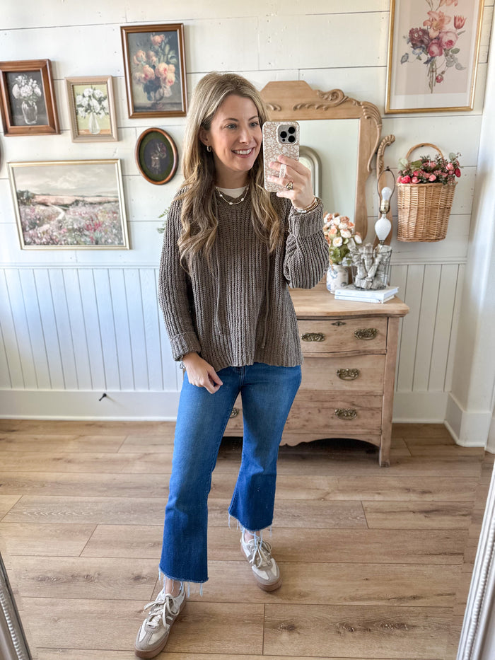 Woman taking a mirror selfie in a room with wooden floor and framed pictures on the wall.