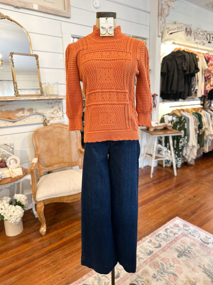 Mannequin wearing an orange sweater and blue pants in a store setting