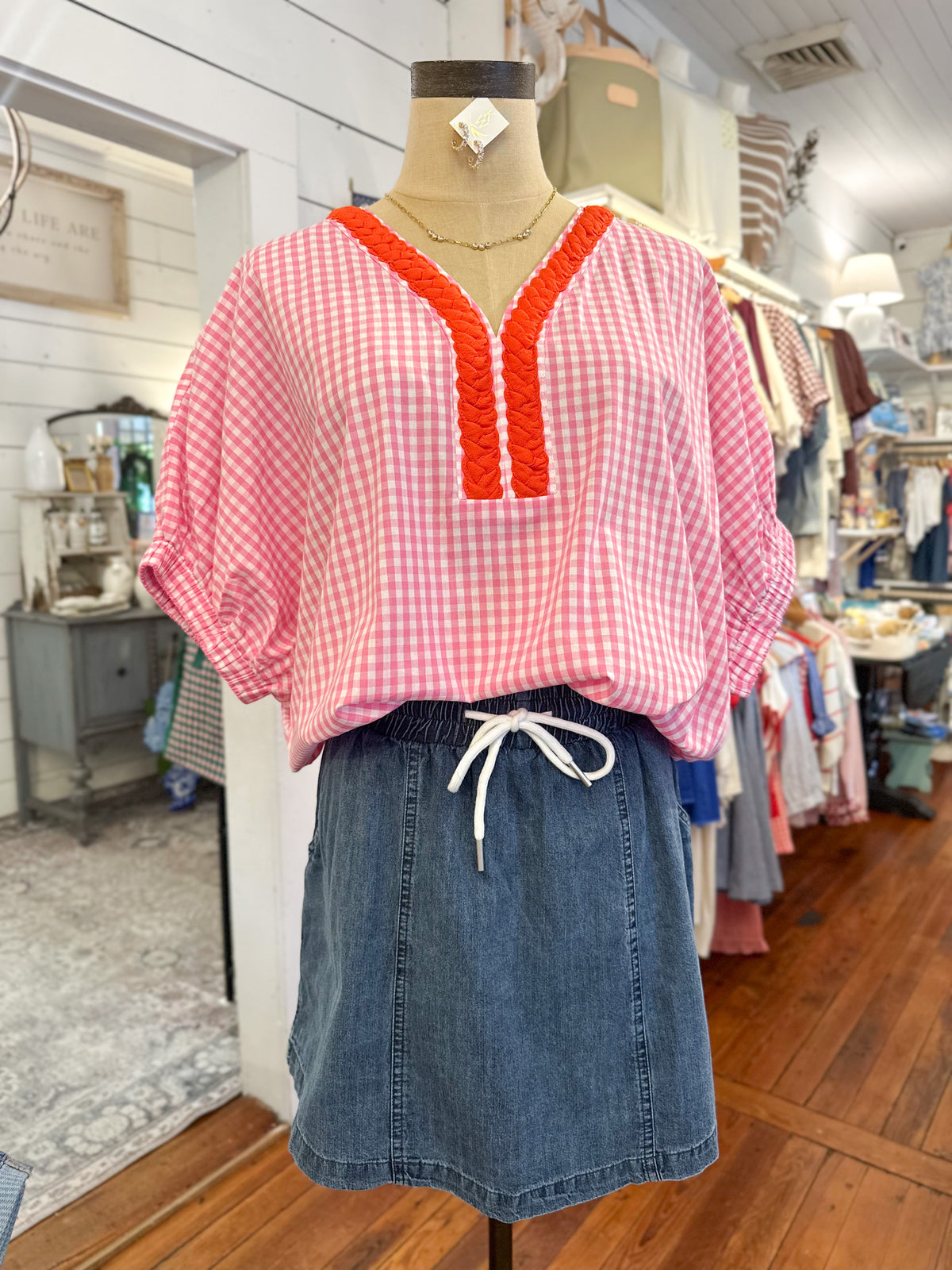 Mannequin wearing a pink checkered top with red trim and a denim skirt in a store setting.
