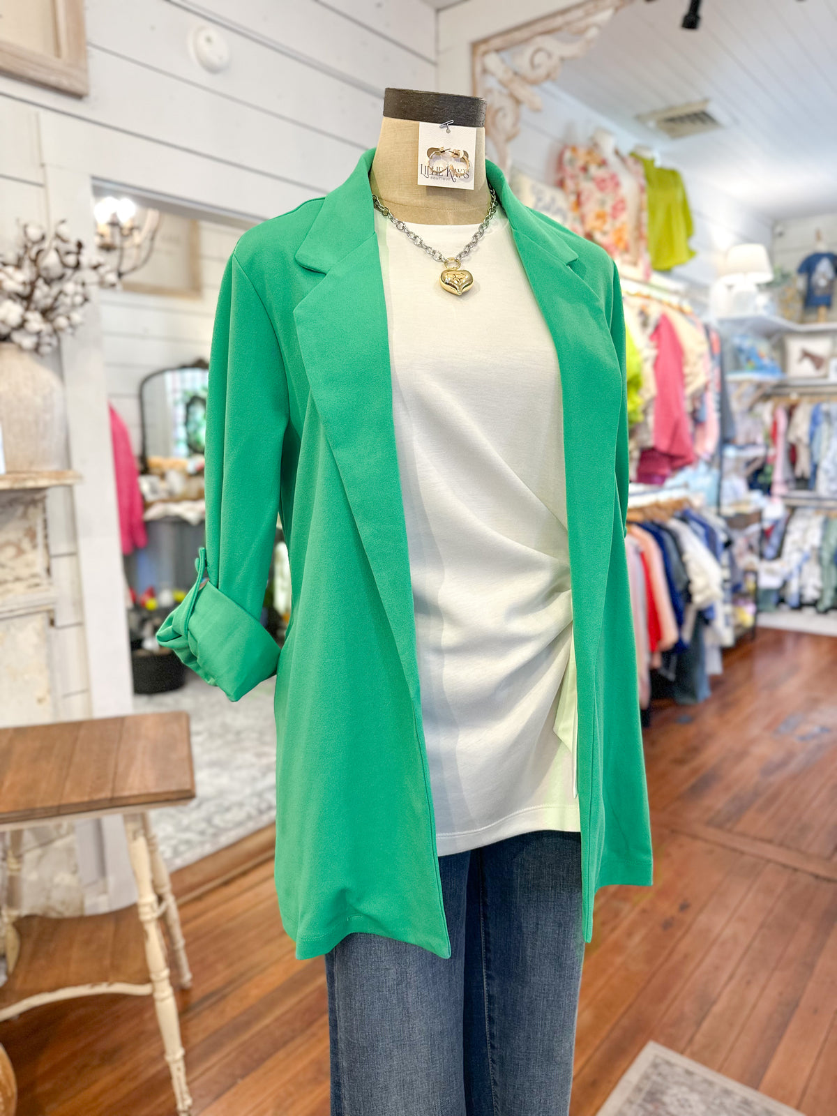 Green blazer over a white top and jeans on a mannequin in a store setting.