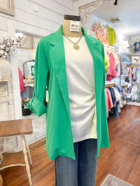 Green blazer over a white top and jeans on a mannequin in a store setting.