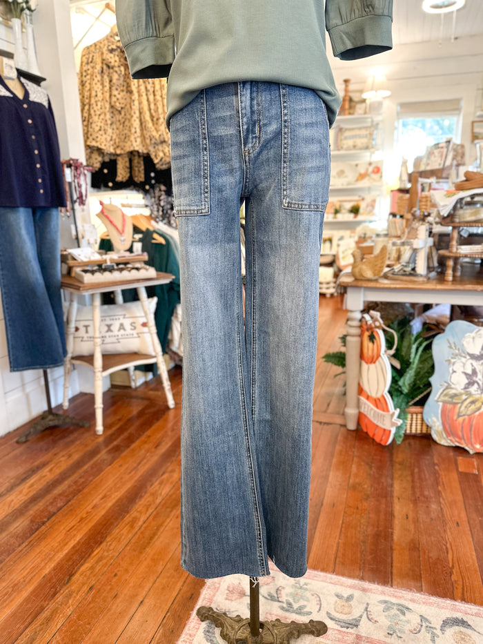 Blue jeans on a mannequin in a store setting with wooden floors and various items in the background.