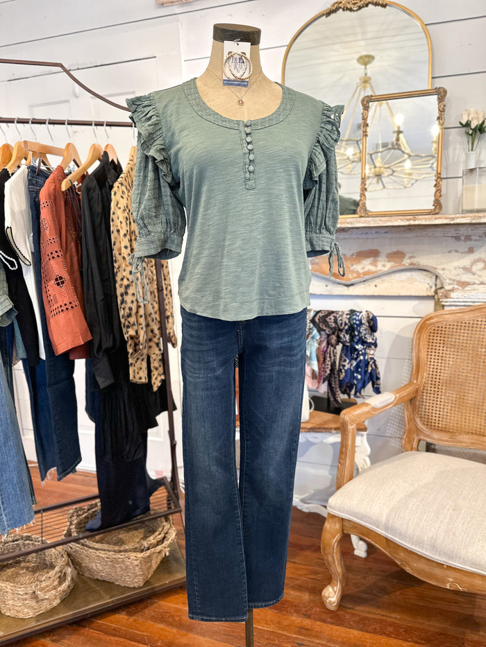 Mannequin wearing a green top and blue jeans in a clothing store setting.