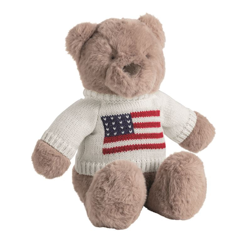 Plush teddy bear wearing a sweater with an American flag design on a white background