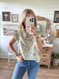 Woman taking a mirror selfie wearing a floral blouse and blue jeans in a home setting.