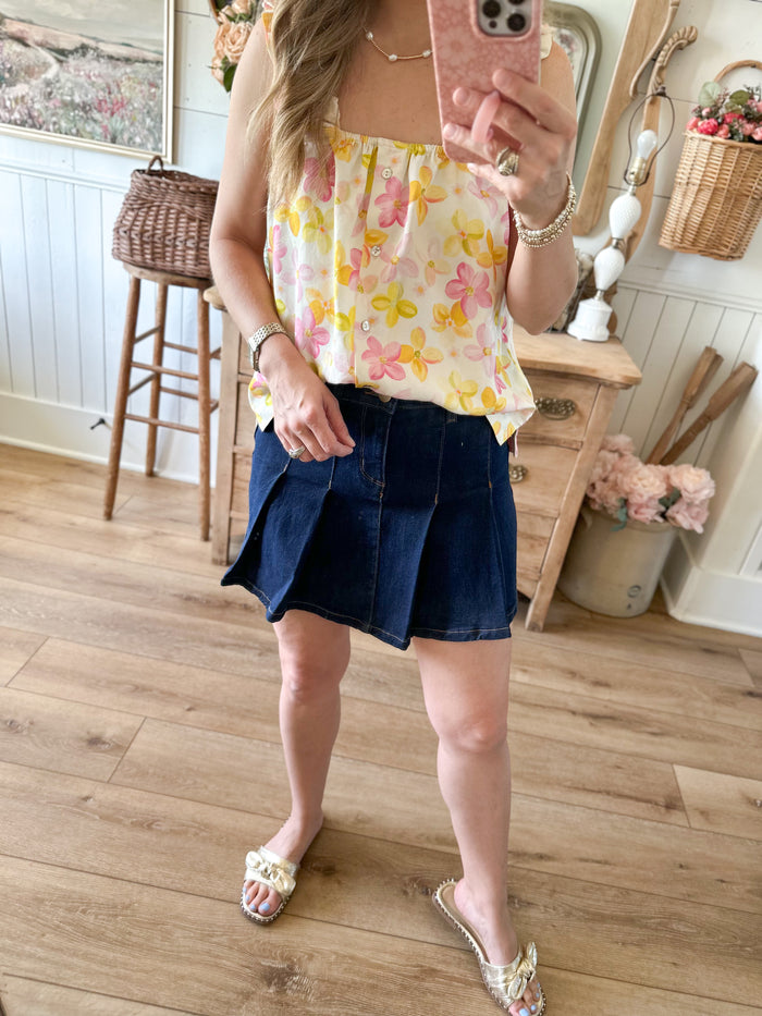 Woman taking a mirror selfie wearing a floral top and denim skirt in a home setting.