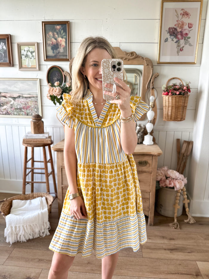 Woman taking a mirror selfie wearing a yellow and white dress in a home setting.