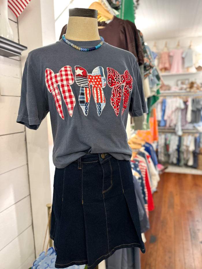 A dark gray graphic t-shirt displayed on a mannequin torso in a clothing boutique. The shirt features a patriotic-themed bow sewn on applique design 