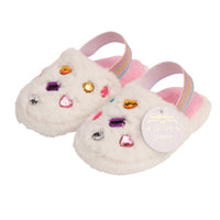 A pair of white fuzzy toddler slippers decorated with colorful rhinestones, featuring pastel pink straps with rainbow stripes and a round white hangtag that reads 'Glitter Slippers'.