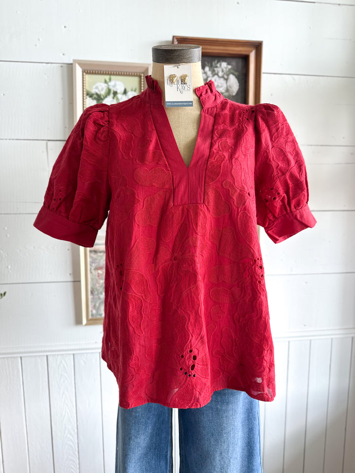Red blouse on a mannequin against a white wall with framed pictures.