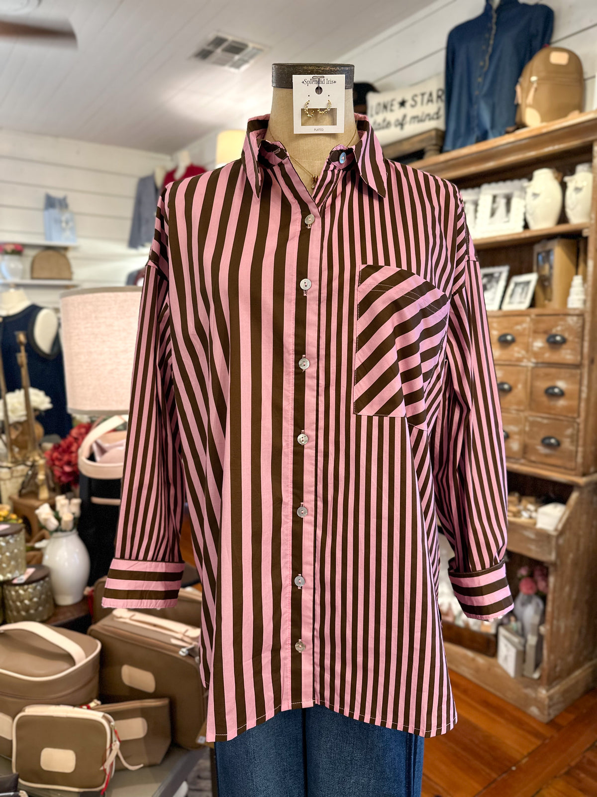 A pink and dark brown vertically striped button-up shirt with a chest pocket, displayed on a mannequin torso inside a retail shop.