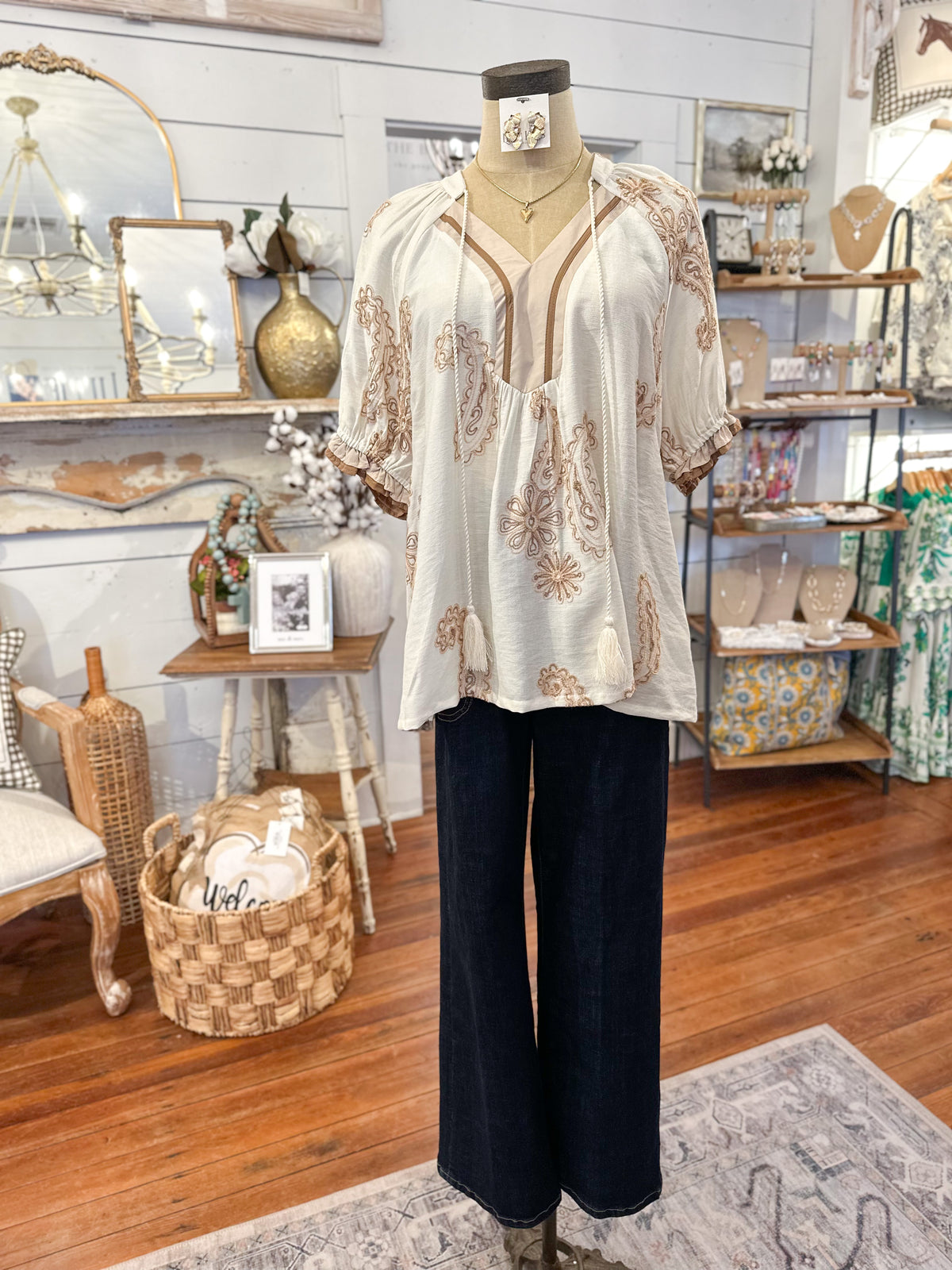 Mannequin wearing a white blouse with brown patterns and black pants in a store setting.