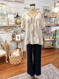 Mannequin wearing a white blouse with brown patterns and black pants in a store setting.