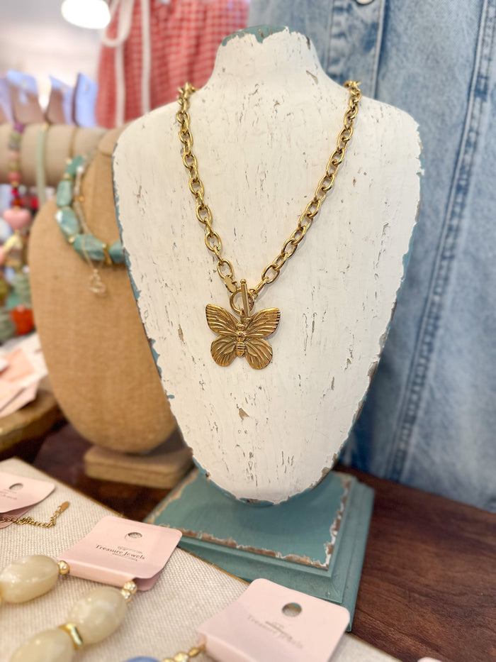 Gold butterfly necklace on a white stand with blurred background