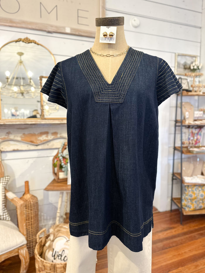 Navy blue denim top on a mannequin in a store setting with decorative items in the background.