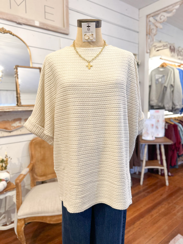 Mannequin wearing a cream-colored short sleeve sweater  in a store setting