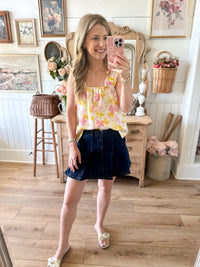 Woman taking a mirror selfie wearing a floral top and dark skirt in a home setting.