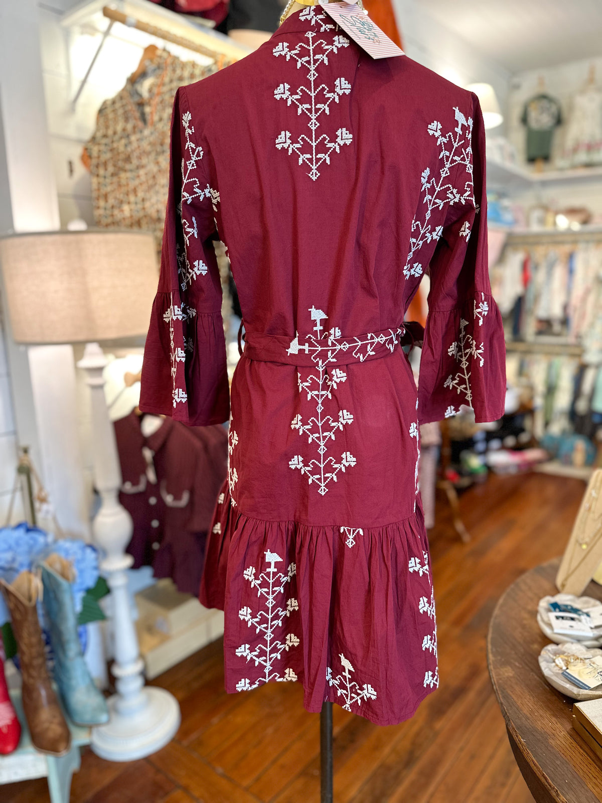 A burgundy long-sleeve mini dress with white floral embroidery, displayed on a mannequin in a boutique setting.