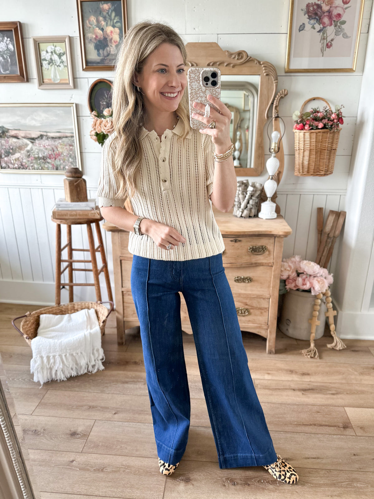 Woman taking a mirror selfie in a room with wooden furniture and decorative items.