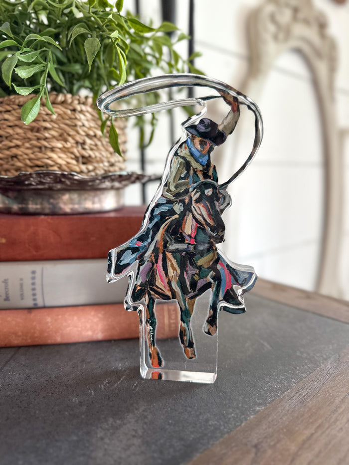 Colorful acrylic sitter of a person riding a horse on a clear stand, with a plant and books in the background.