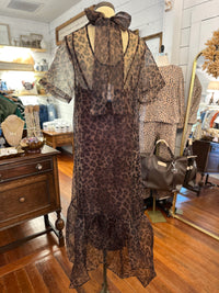 A leopard-print sheer mesh dress displayed on a mannequin in a boutique. The dress features a brown and black animal print with a matching sheer bow at the neckline and short sheer sleeves.