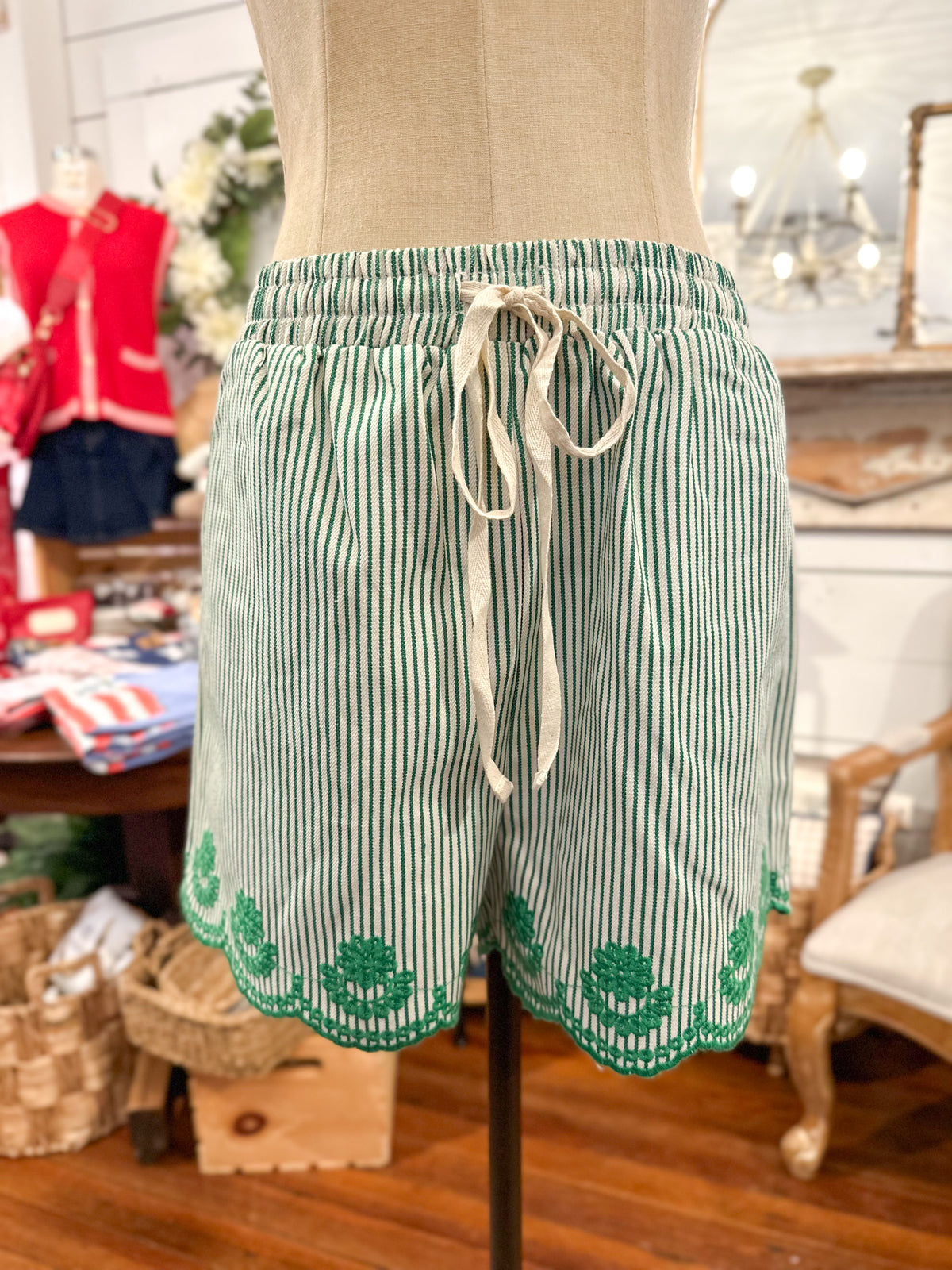 Green and white striped shorts with a drawstring on a mannequin in a store setting.
