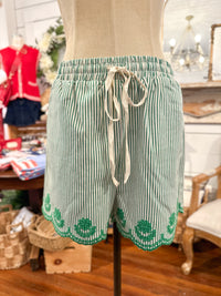 Green and white striped shorts with a drawstring on a mannequin in a store setting.