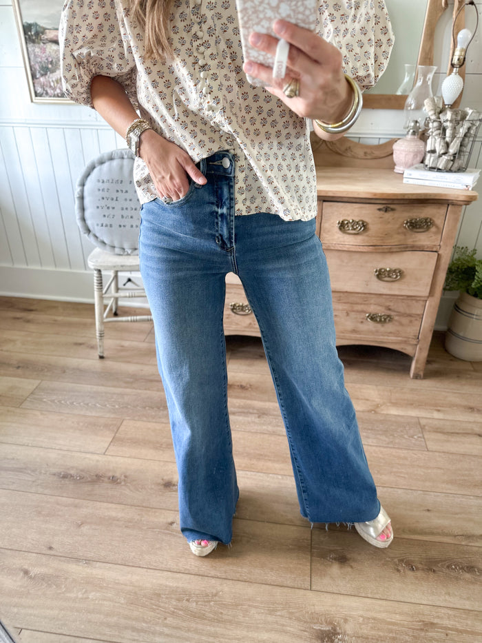 Person wearing a patterned blouse and blue jeans indoors.