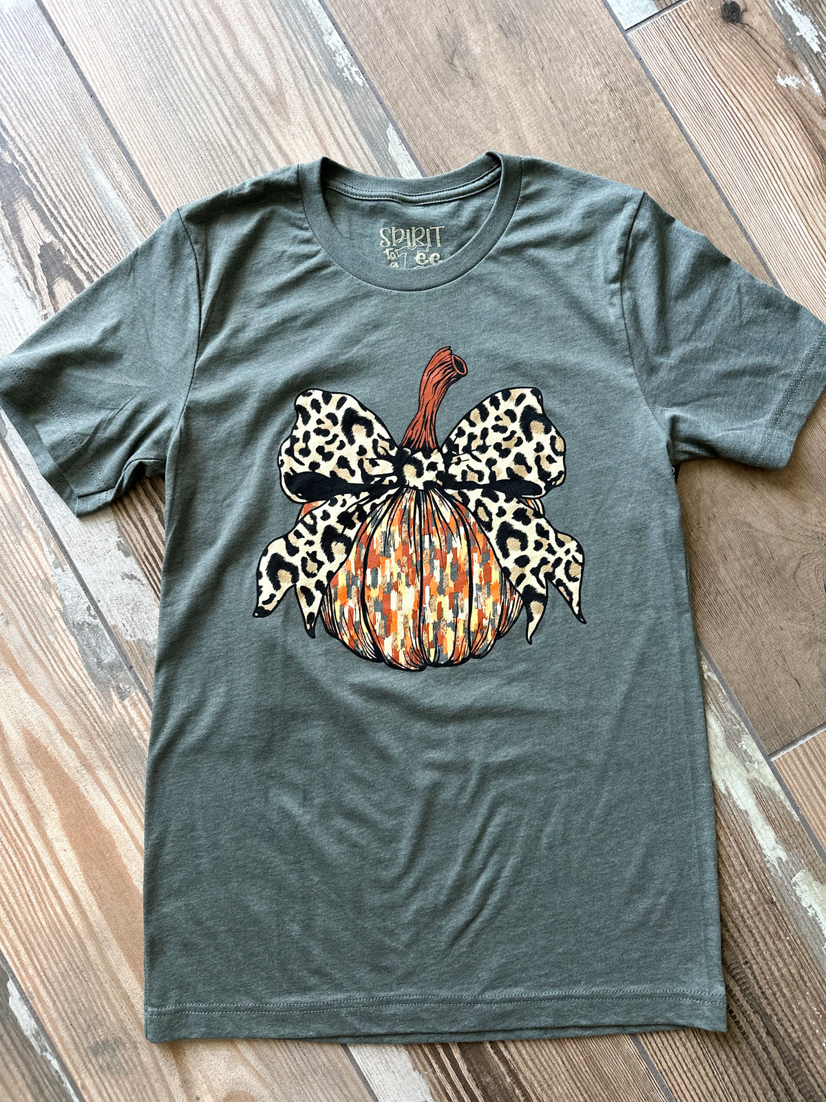 Green t-shirt with a leopard print pumpkin design on a wooden surface