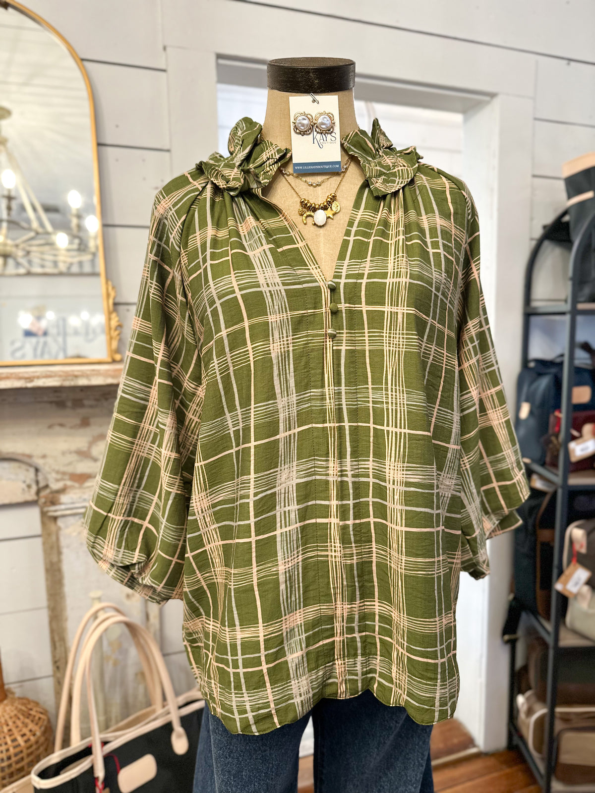 green plaid blouse with cream stripe pattern ruffle detail around neckline inside store setting 