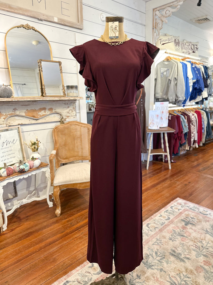 Maroon pant jumpsuit on a mannequin in a store setting with mirrors and clothing racks.