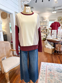 Mannequin wearing a cream and burgundy sweater with blue jeans in a store setting.