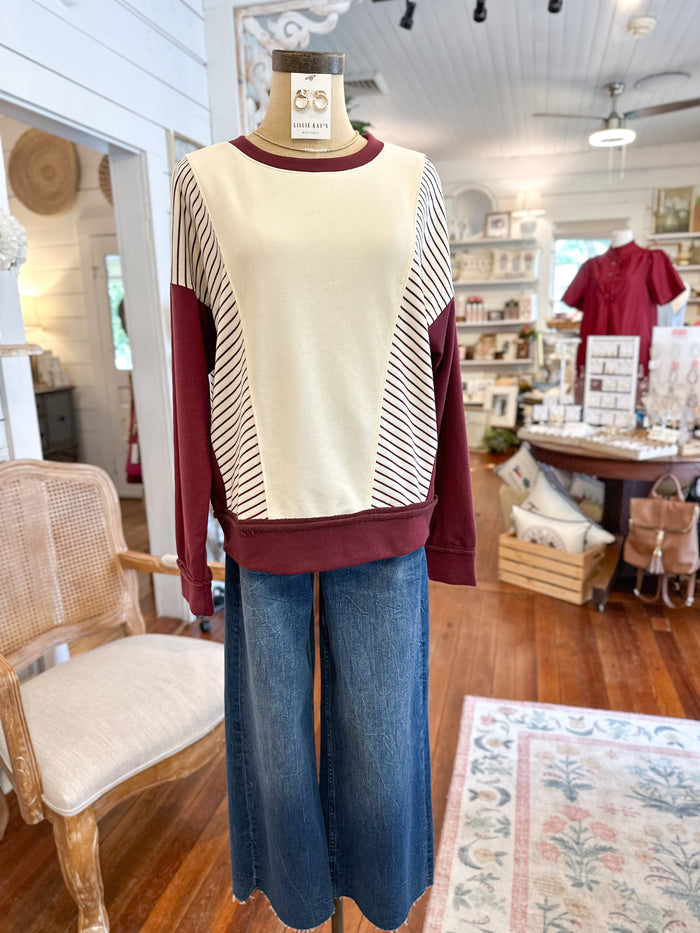 Mannequin wearing a cream and burgundy sweater with blue jeans in a store setting.