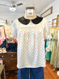 White blouse with black polka dots and collar on a mannequin in a store setting.