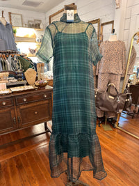 A dark green plaid midi dress with sheer short sleeves and a ruffled hem, displayed on a mannequin inside a boutique.