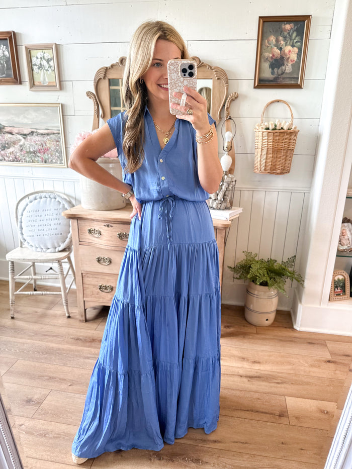 Woman taking a mirror selfie wearing a blue dress in a home setting. satin like maxi dress with tie at waist
