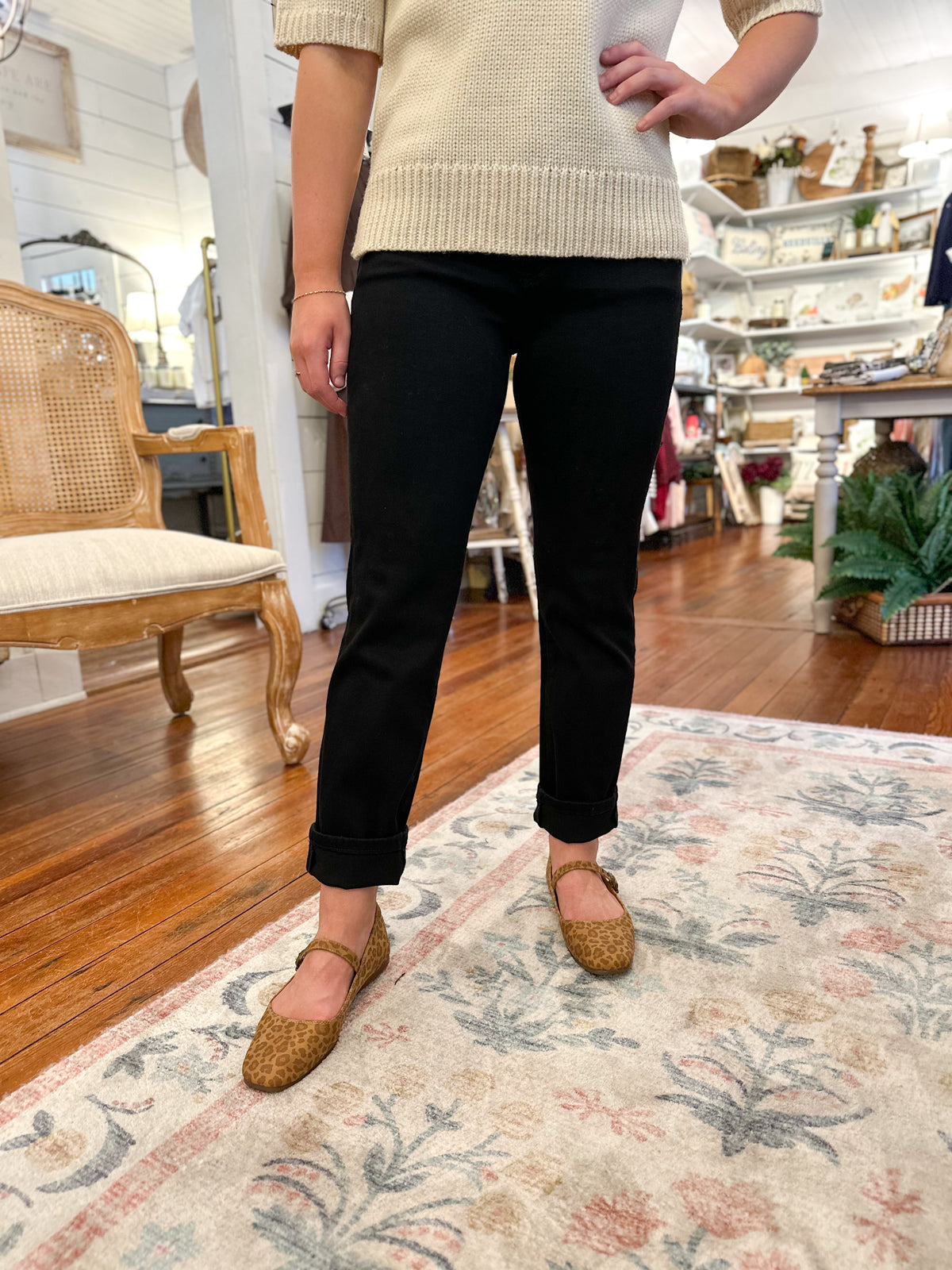 Person wearing a beige sweater, black pants, and leopard print flats in a home setting.